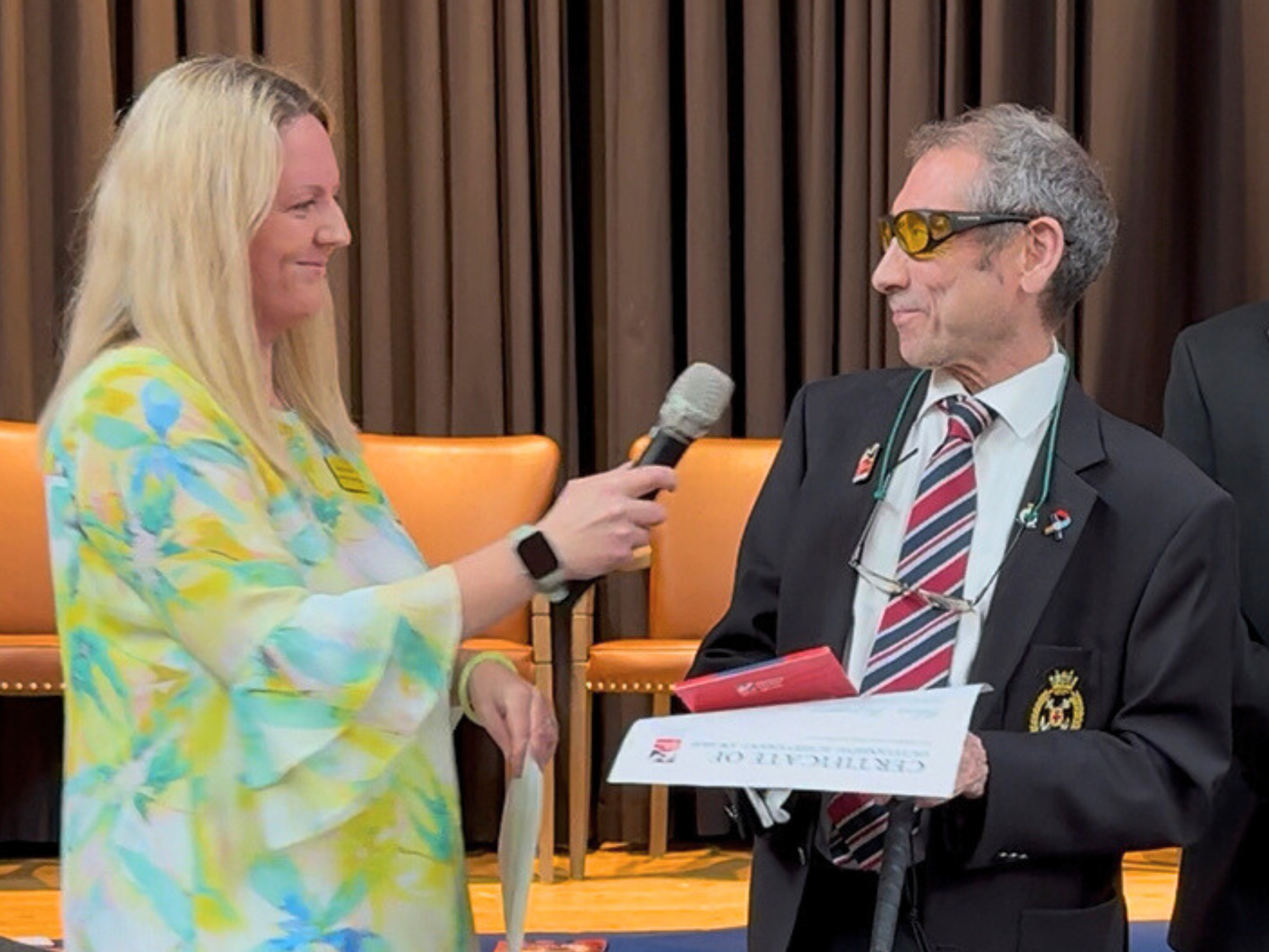Support Worker Nicola holds a microphone up to Chris as he accepts his award.