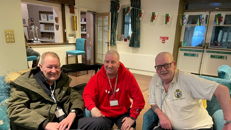 Left to right, Stuart, John, and Jim pictured smiling and sitting down on a sofa and chairs together