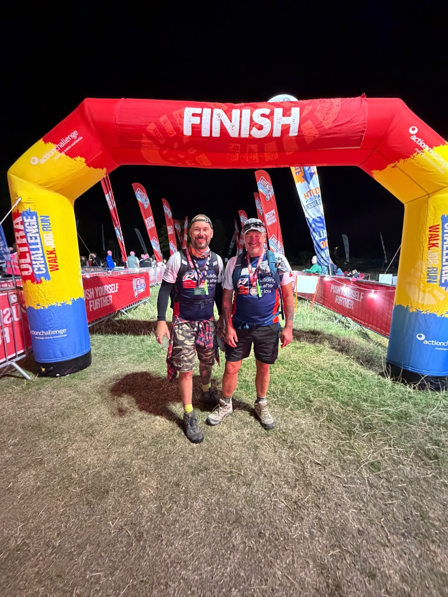 Kark and Aaron stand beneath the finish arch in the dark