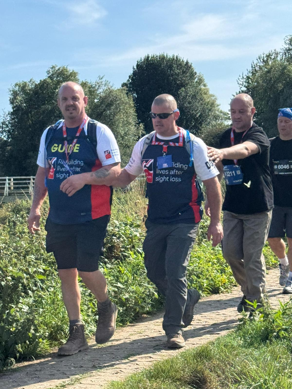 Stu holding on to the arm of Dave as they make there way along with additional support from volunteers behind him