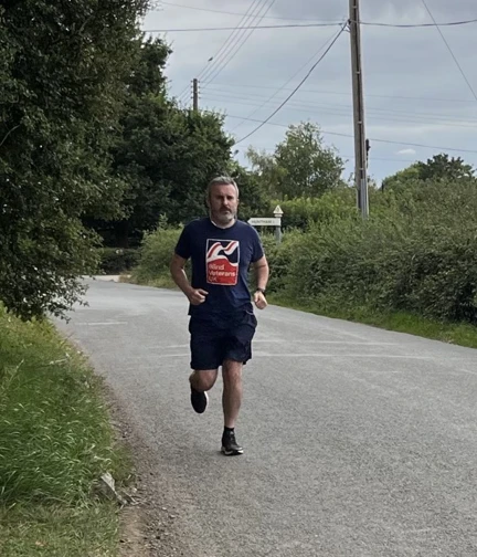 Matt is running along a country road wearing his Blind Veterans UK t-shirt