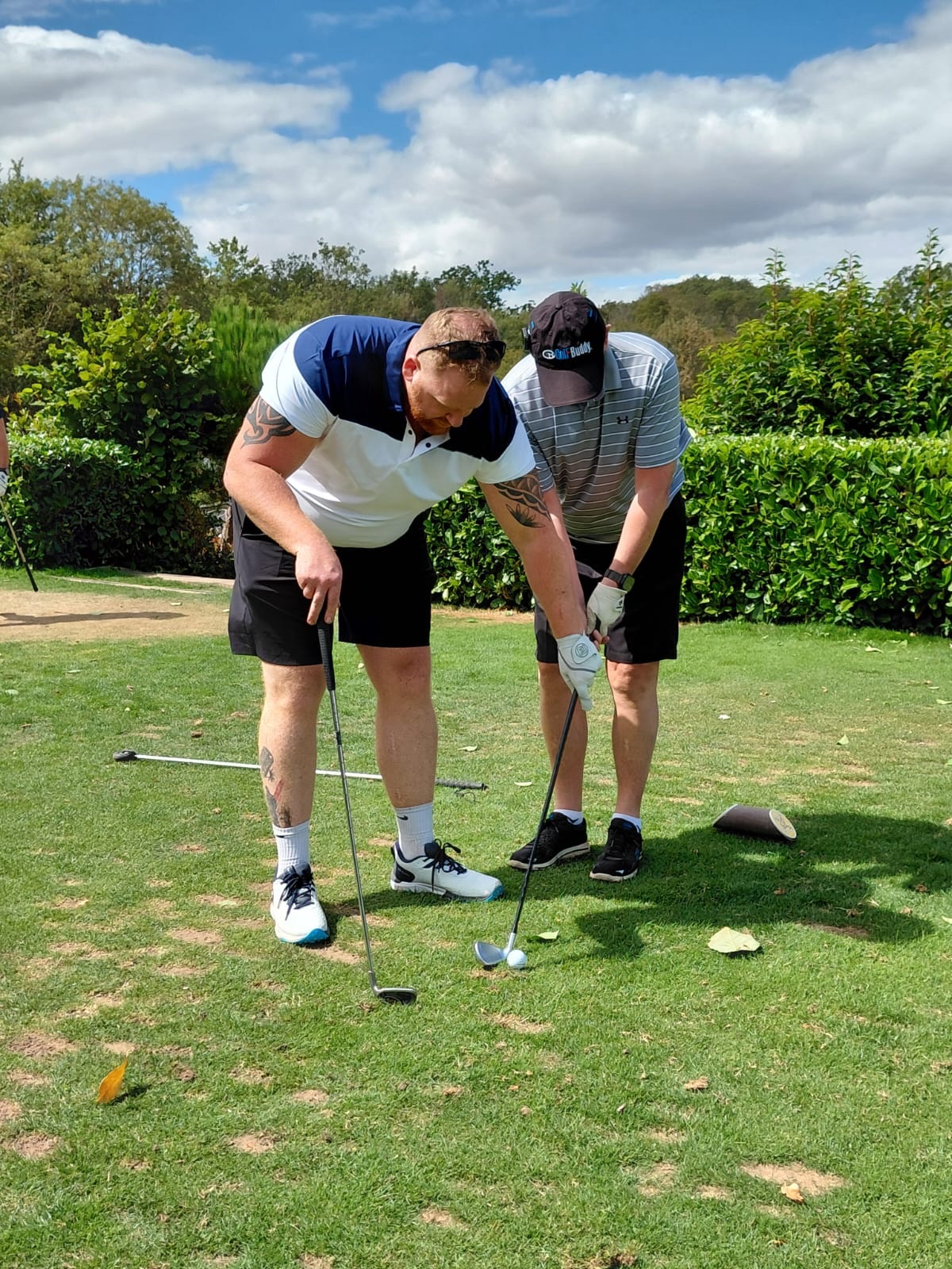Sean stands beside Kev on the tee and uses a golf club to help him establish the direction of his shot.