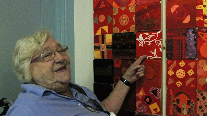 Blind veteran, Win, smiling and pointing to her tile in the Collaboration in Colour artwork