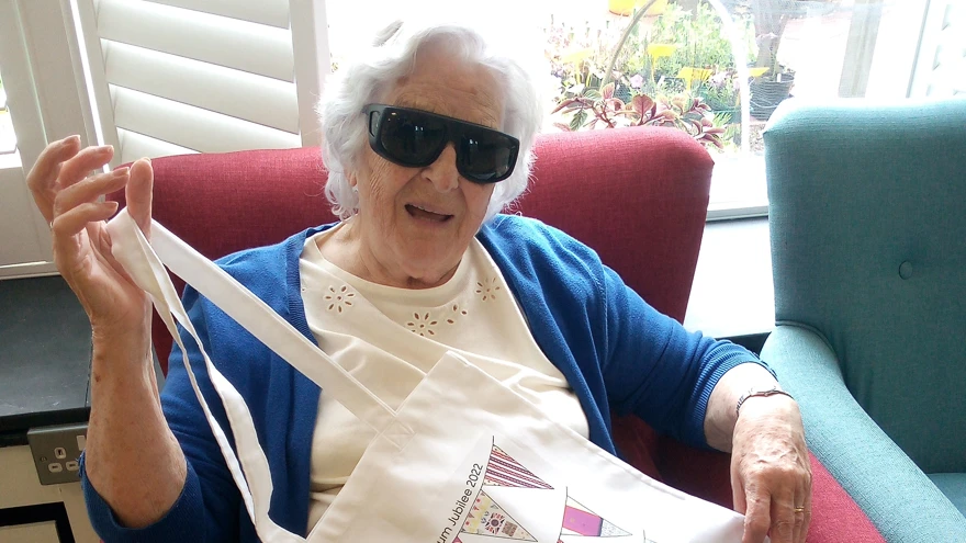 Blind veteran Betty pictured sitting down on a chair holding up her jubilee bunting bag