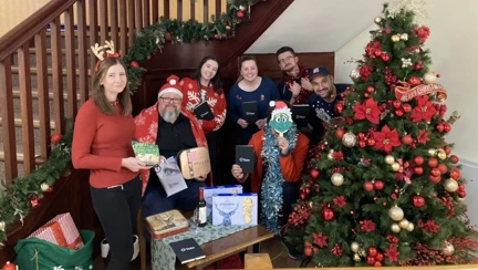 A group of people in front of a Christmas tree and a table of gifts