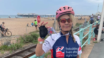 Rider Emilia in her Blind Veterans UK cycling top holding her medal up proudly. The beach and Brighton Pier can be seen in the background.