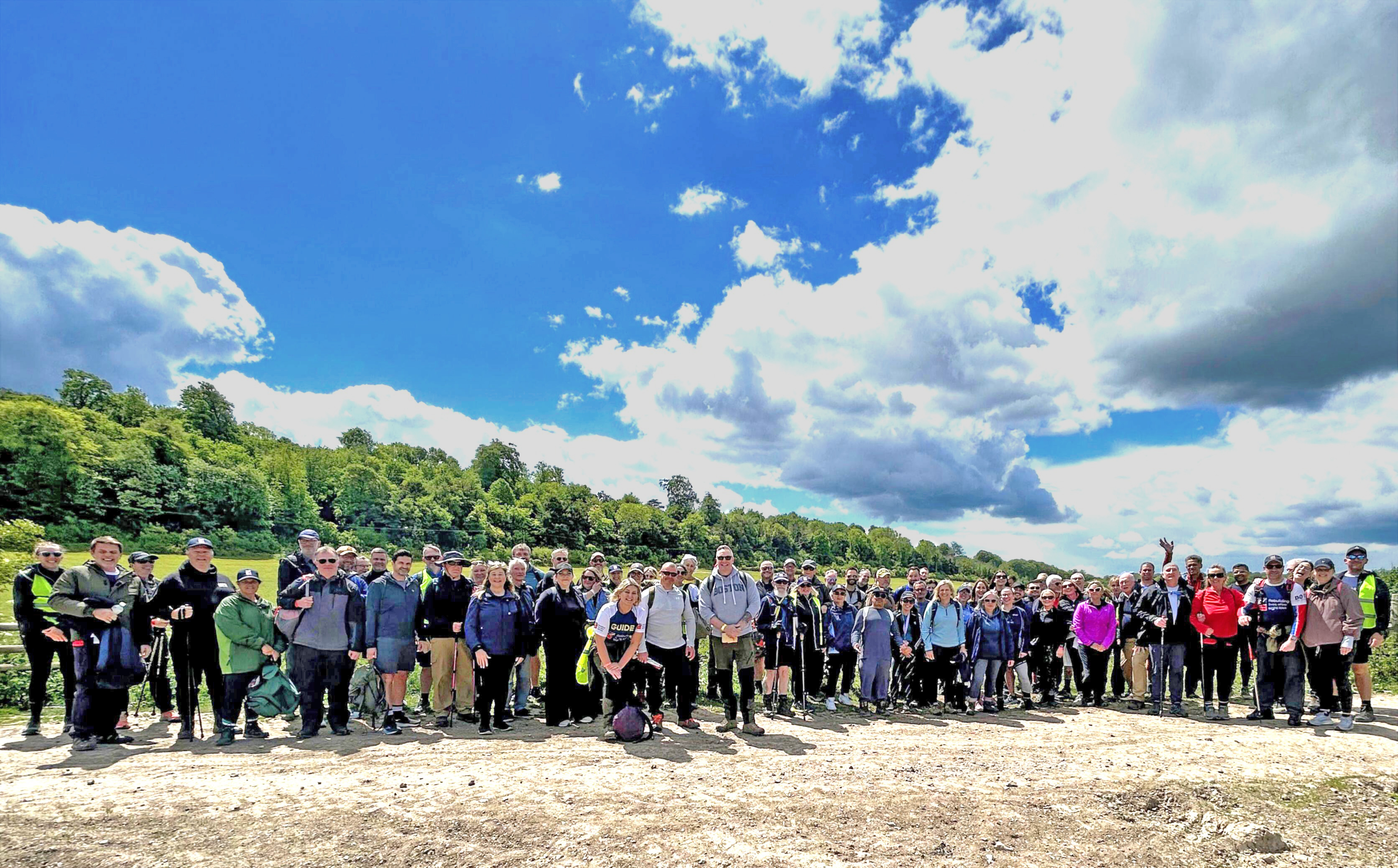 A large group of Operation Enigma participants standing together outdoors beneath a blue sky filled with clouds.