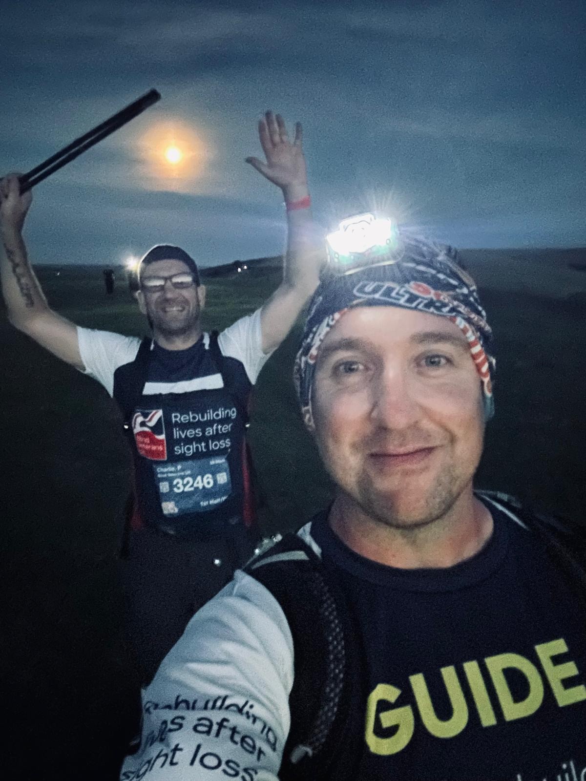 Rich and Charlie are still smiling in the darkness. Rich has a headlamp to help them guide their way and Charlie is in the background with both hands in the air 
