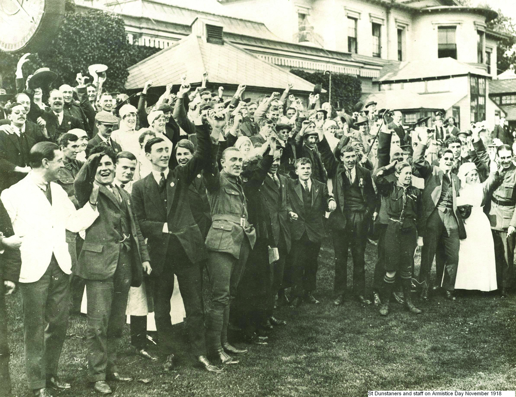 Black-and-white archive photograph of a large group gathered outside the St Dunstan’s building in Regent’s Park on Armistice Day 1918. Many have their arms raised, and several are wearing military or nursing uniforms.
