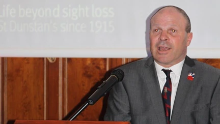 Blind veteran Billy at a podium making a speech at Founders Day event