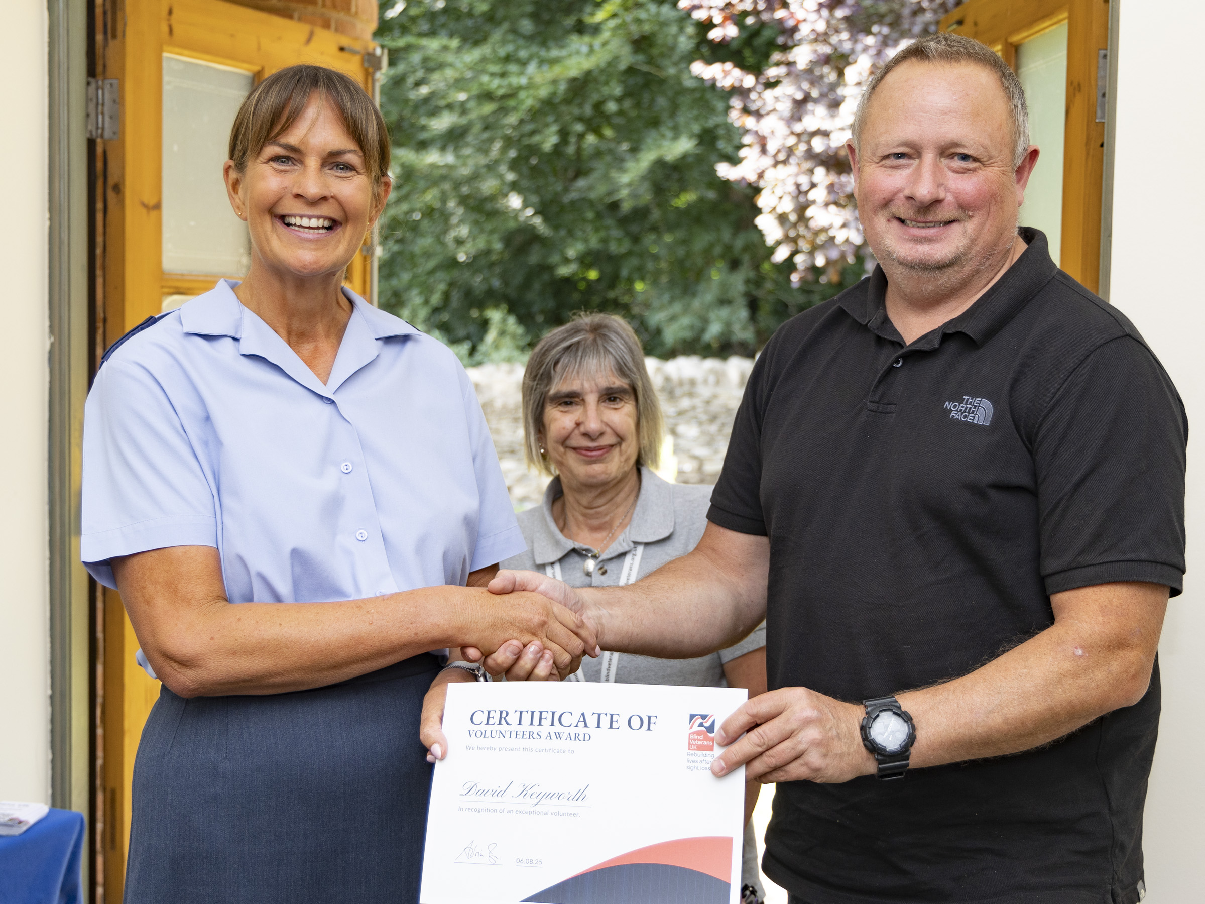 David shakes hands with WO Tracey Kenworthy as she delivers his certificate. Community Supporter Worker Chris stands in between them. They are all smiling. 