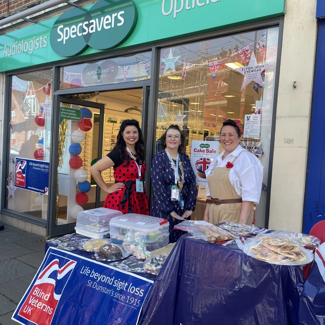 Specsavers in Dorking with a table set up outside for a VE Day 80 cake sale. The store is decorated with red, white and blue balloons and bunting