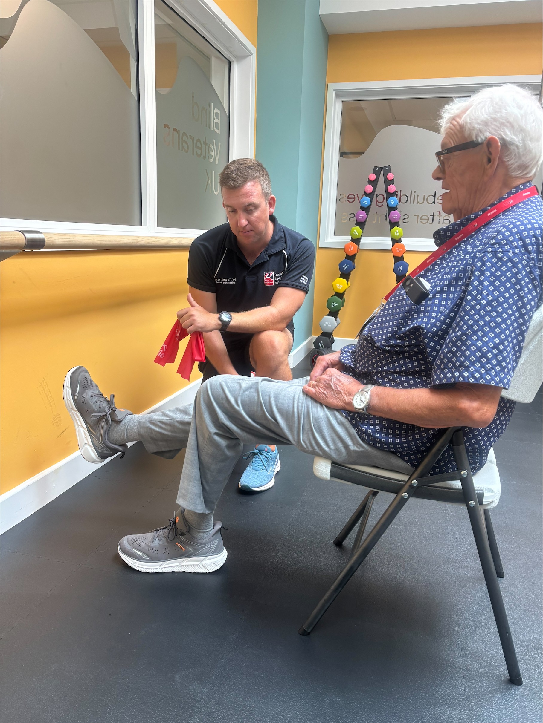 Richard sat on a chair while a member of staff supports him with exercises