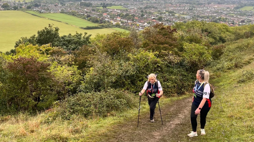 Jill and Ellie climbing up hill on a muddy pathway. Jill is using hiking sticks