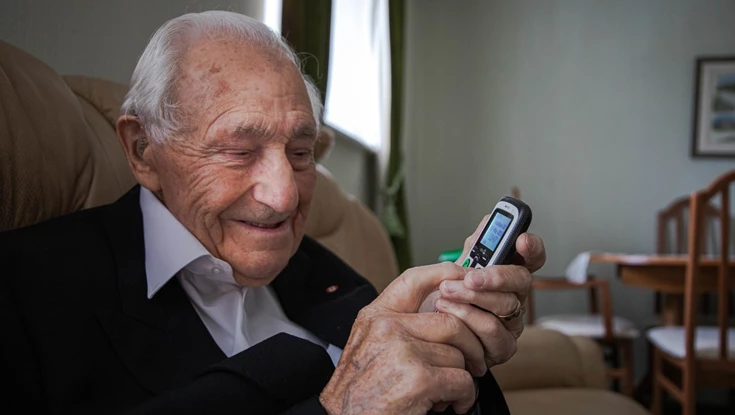 Blind veteran Ron in his living room, smiling as he holds a phone