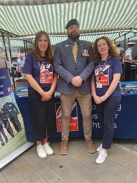 Team member Simon stood in the centre in his military blazer, beret and medals.  Two team members are either side of him in their Blind Veterans UK tops.