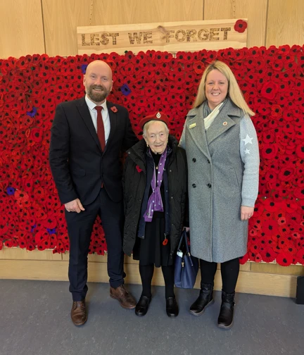 A blind veteran standing with two staff members in front of a wall of poppies