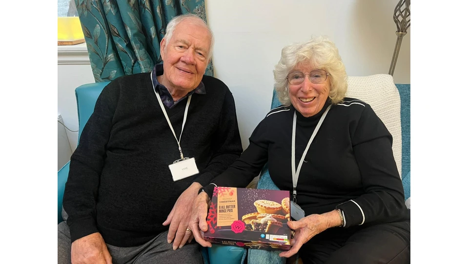 A couple sitting in armchairs with a box of mince pies