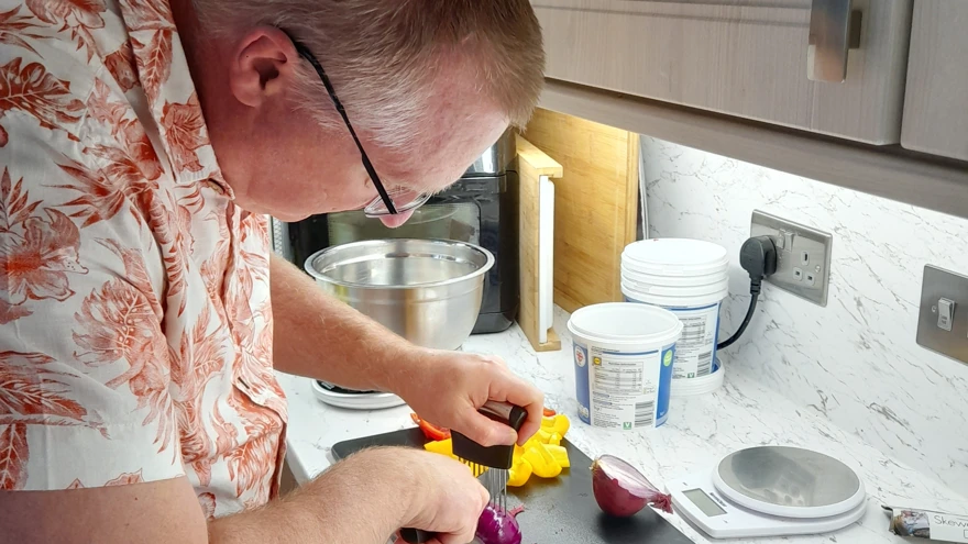 Rob stood at his kitchen sideboard safely using a knife and cutting guide to slice an onion