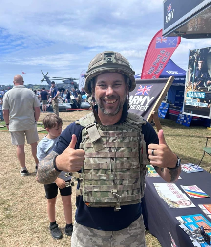 Aaron giving a thumbs up, smiling, dressed in army camoflauge