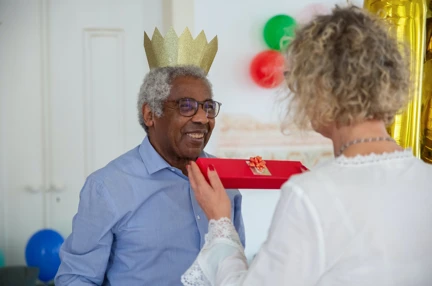A woman handing a wrapped gift to a man wearing a Christmas hat
