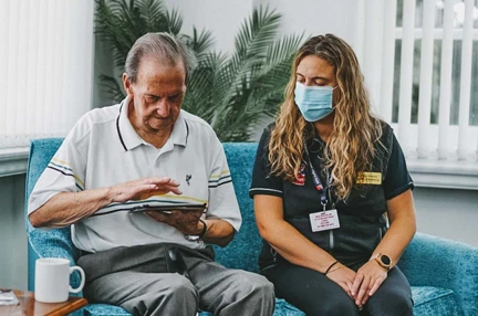 Blind veteran veteran Fred using a tablet, while sitting on a sofa with a Blind Veterans UK staff member