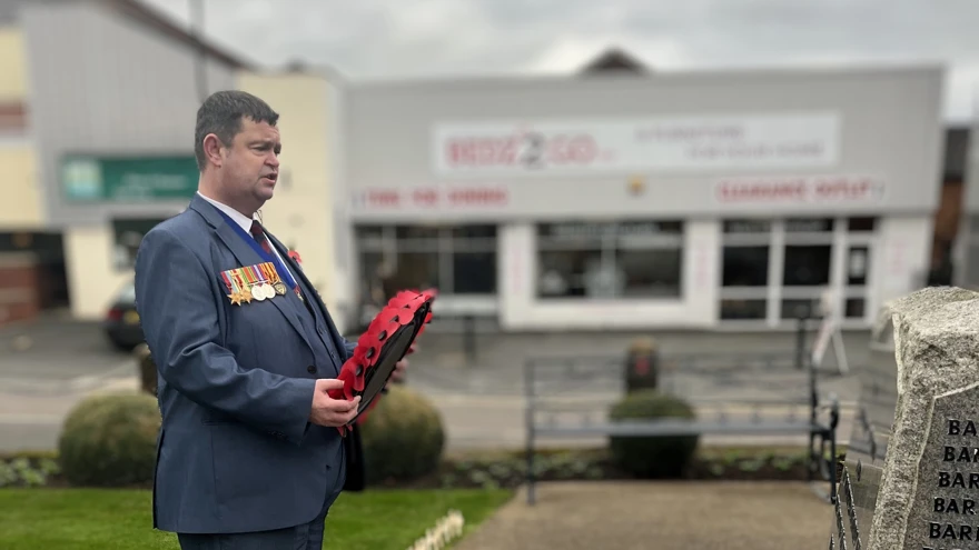 Clive wears a blue suit with medals attached and is holding a poppy wreath in a moment of reflection ahead of placing it at the Market Drayton War Memorial
