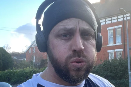 Matt wearing a Blind Veterans UK T-shirt and headphones at the end of a training run looking tired