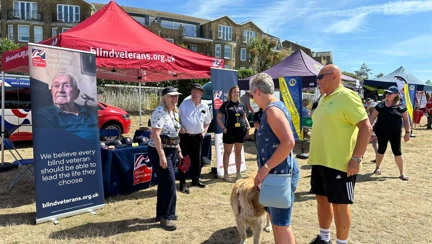 A Blind Veterans UK gazebo and stall, decorated with banners and merchandise with a small crowd gathered round