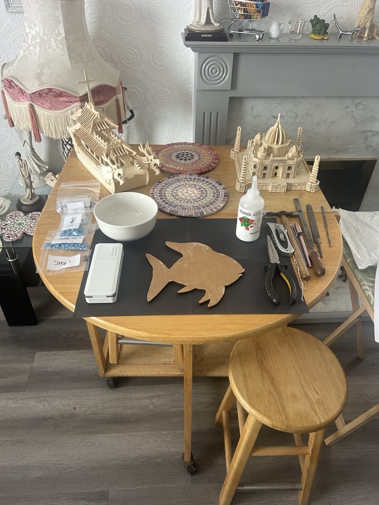 A simple table and stool set up with different mosaics and wooden projects laid out.
