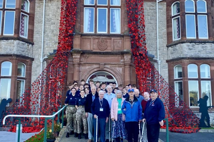 A group of veterans and volunteers stand outside the entrance of our Llandudno Centre, which is decorated with the cascading poppy blanket