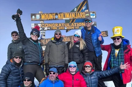 Ian alongside the other climbers all smiling under the Mount Kilimanjaro peak sign