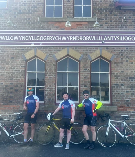 The three cyclists stood next to their bikes under the sign for Llanfairpwllgwyngyllgogerychwyrndrobwllllantysiliogogogoch