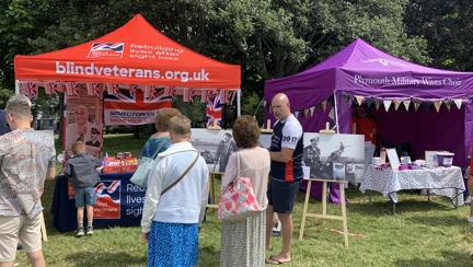 A Blind Veterans UK stall at Armed Forces Day, with several people standing in front of it speaking to staff