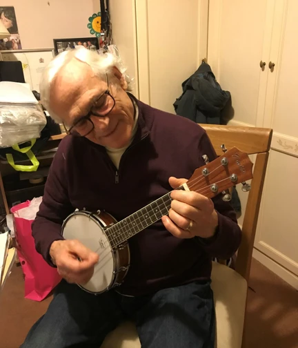 Sydney sat on a dining chair playing his ukulele with a smile on his face