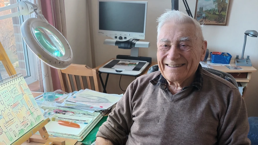 A photo of blind veteran Bill, pictured smiling and sitting next to his artwork