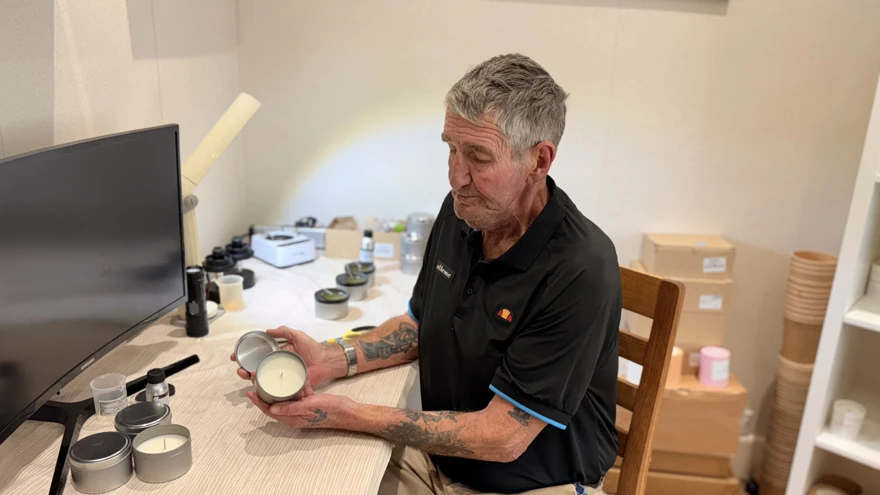Tony at his desk during the candle making process. Behind him are three candles which he has just poured and he is holding a candle that has set but is yet to be labelled.