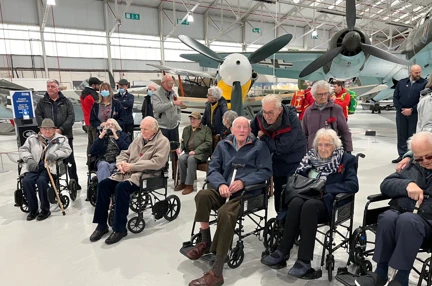A photo of a group of blind veterans visiting the RAF Cosford Museum posed in front of the fighter jets