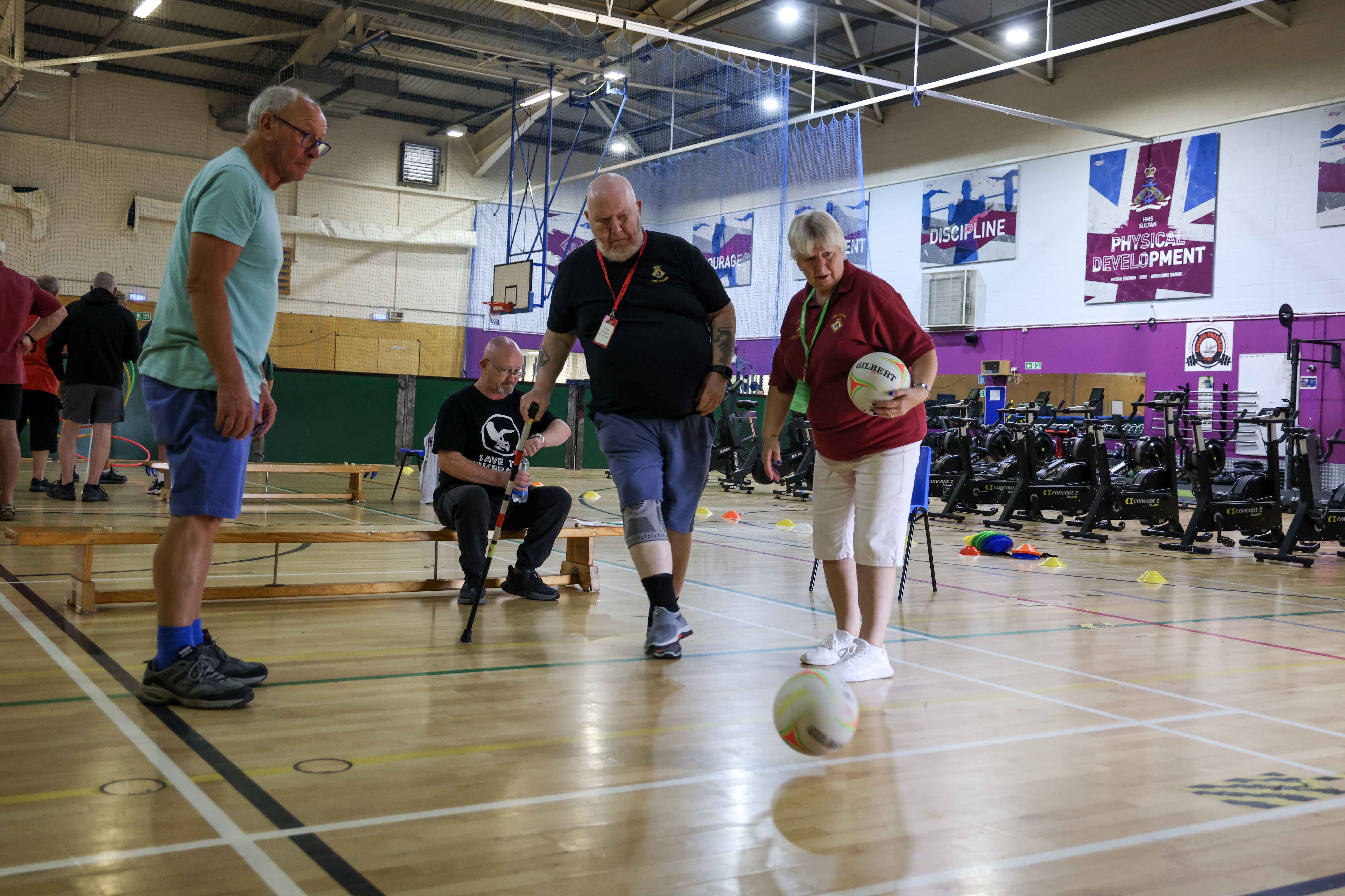 A blind veteran kicks a football, supported by two guides