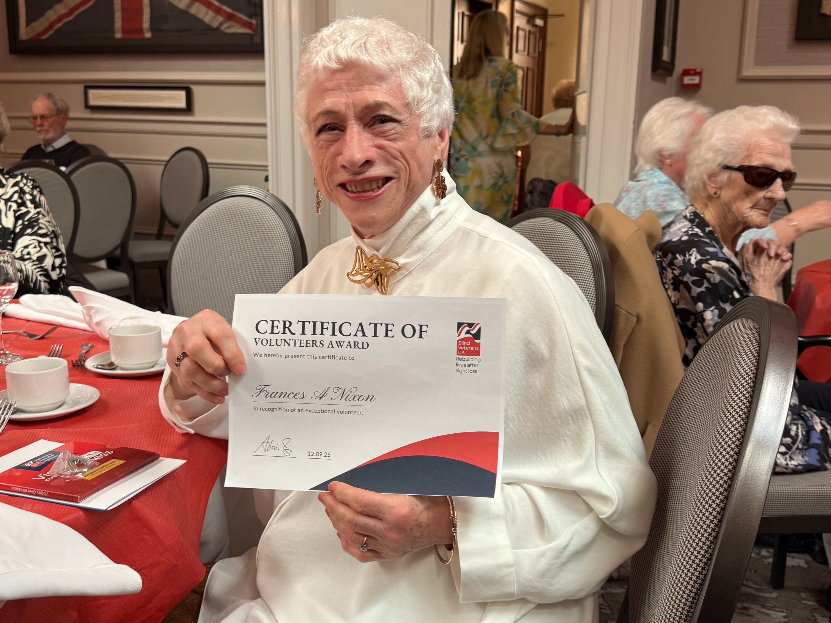 Frances is seated at a table and smiling as she holds her certificate.