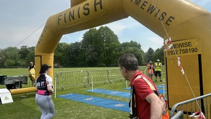 Megan jogging towards a large yellow inflatable arch which is the finish line