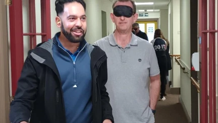 A man wearing a blindfold is holding the arm of another man while he is guided around the inside the the Llandudno Centre