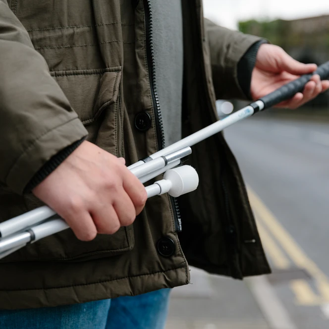 A man's hands holding a folded white cane
