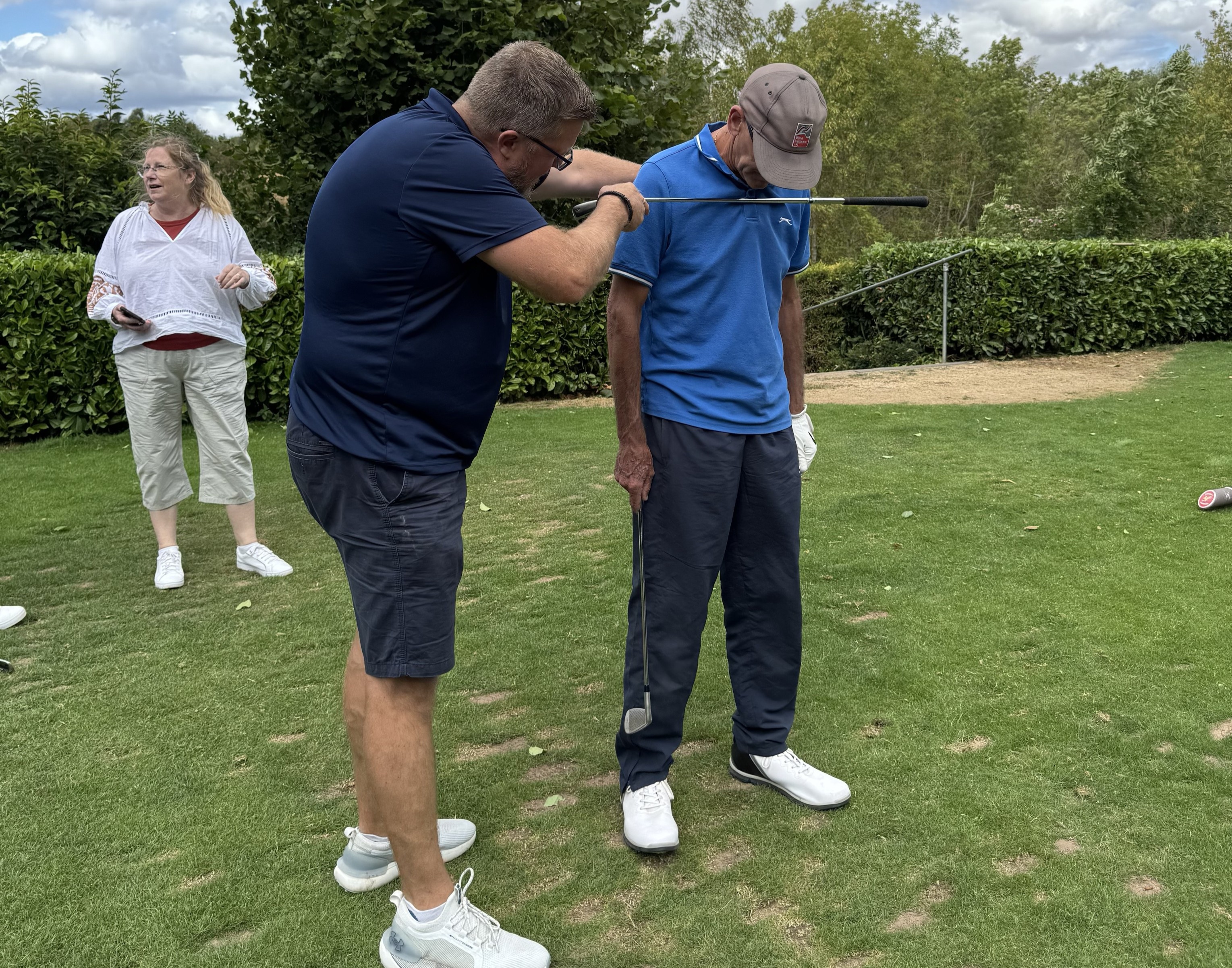 SUEZ participant Grant demonstrates golf club positioning to blind veteran Steven on the driving range.