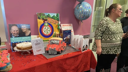 A table displaying a birthday cake, cards and balloons at blind veteran Ken's 100th birthday
