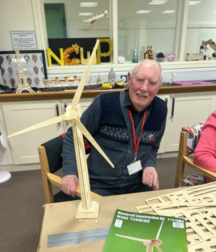 Rob sits at a table behind a wooden model of a wind turbine