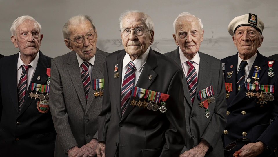 Seven blind veterans edited alognside each other over a sepia back of a beach on D Day