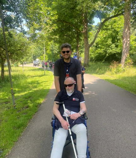 Sam pushing Dean in a wheelchair along a tree lined path.