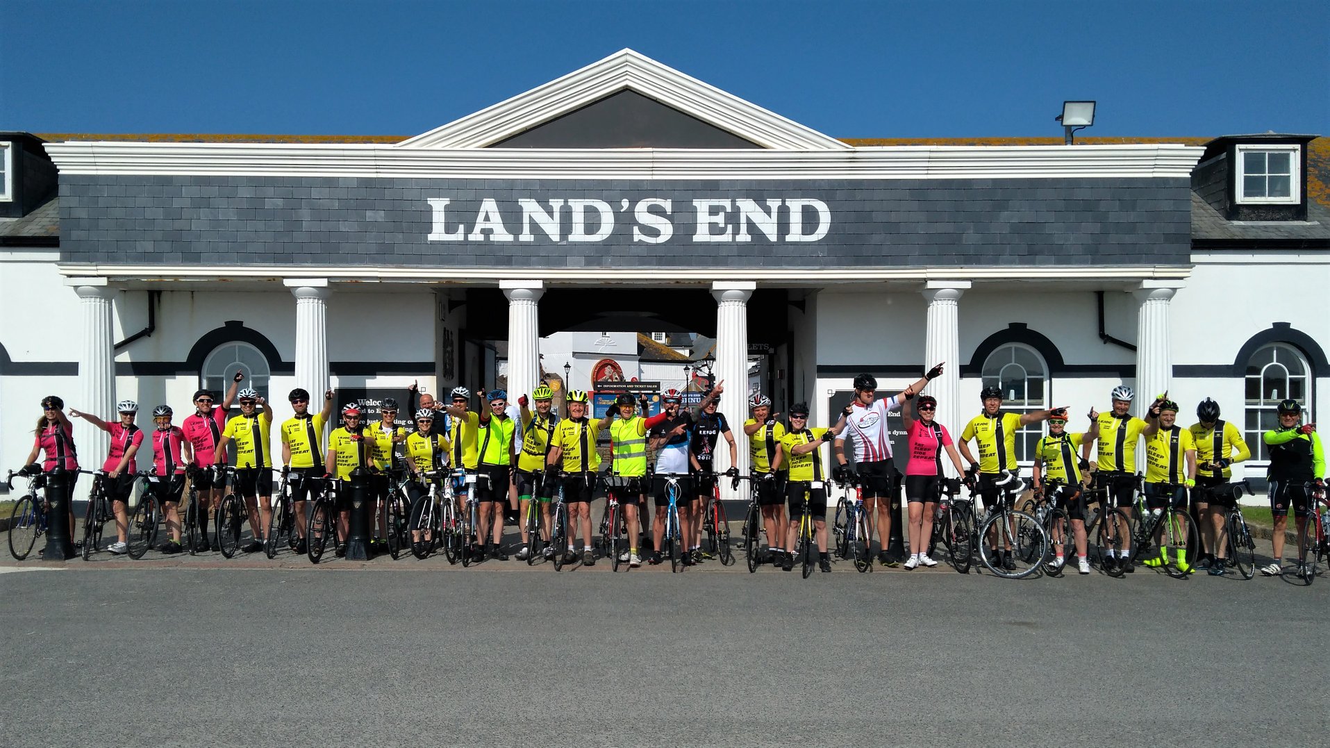 A group of cyclists on their bikes under the Lands End sign.