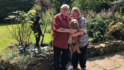 Danny and Carol stood in their garden holding their cockapoo between them